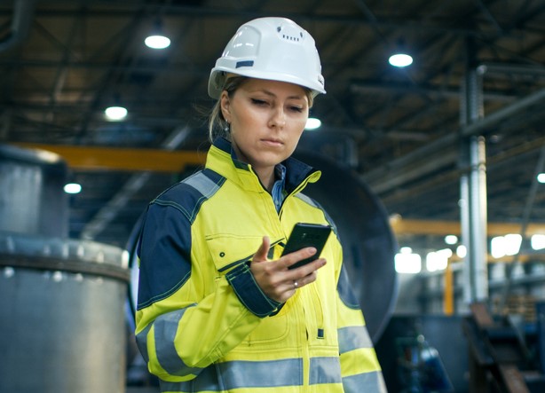 woman in manufacturing building looking at cell phone and safety app